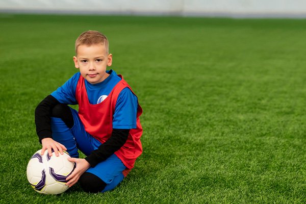 Young soccer player sitting on the field with a ball at CJ Lasso Arena